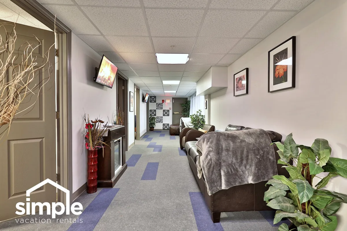This image features a welcoming living area with comfortable sofa seating, decorative plants, wall art, and a television. The space is arranged to encourage casual conversation and relaxation, ideal for guests who want to unwind between event festivities.