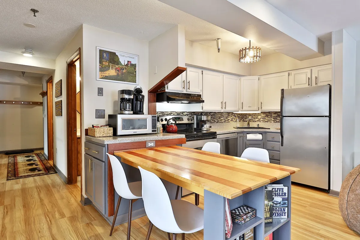 A modern kitchen with a prominent island, stylish appliances, decorative lighting, and comfortable dining chairs. Sunlight filters in, creating a bright and inviting space ideal for morning coffee or entertaining guests.