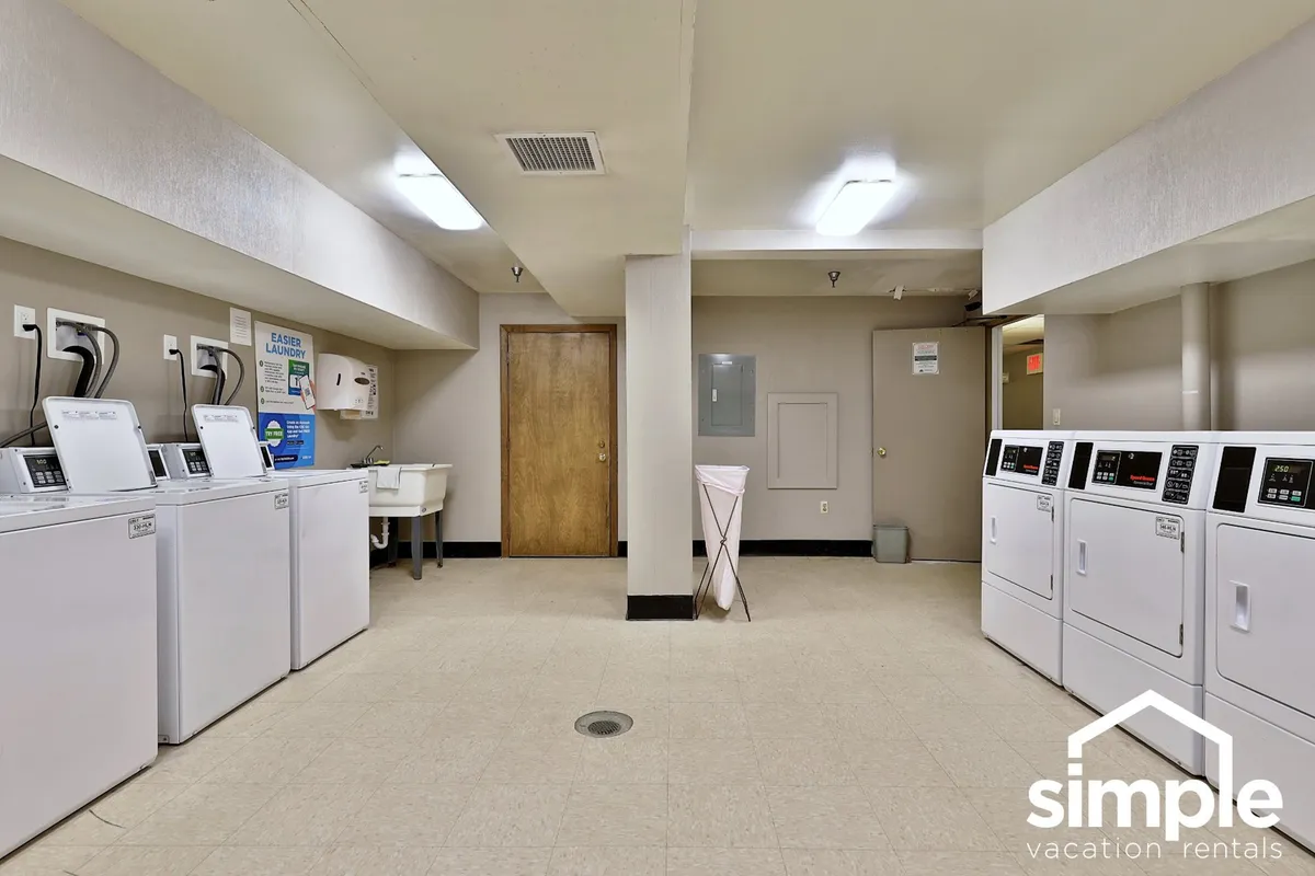 A practical utility space with multiple washing machines, dryers, a utility sink, and a doorway leading outside. The clean, functional setup showcases the communal laundry facilities available to guests.