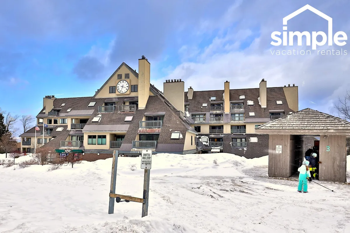 The exterior of a lodge building with a prominent clock, surrounded by fresh snow. Guests are seen engaging in various winter activities such as skiing and snowball fighting, while others relax near the entrance, evoking a cheerful, adventurous après-ski atmosphere.