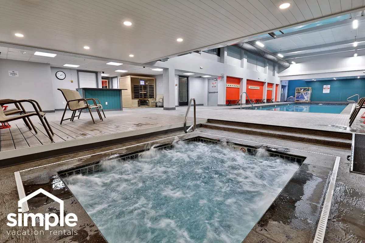 This image features an indoor swimming pool paired with a hot tub and lounge chairs, offering a calm, rejuvenating atmosphere. Guests can be seen relaxing in the hot tub or chatting poolside, highlighting the wellness and social aspects of the resort’s amenities.