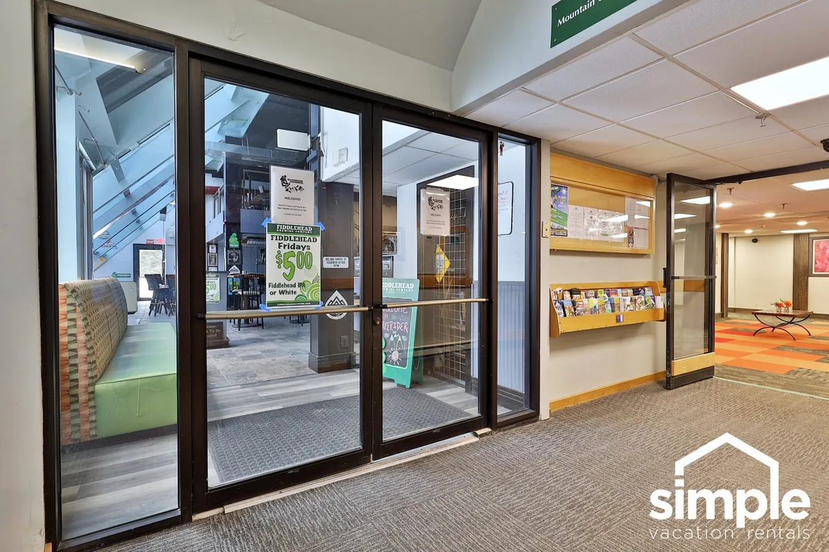 This image features the glass entrance doors of the condo complex, a cheerful green seating area, and an information display. Guests are seen greeting each other and browsing local information, capturing the resort’s welcoming lobby and the sense of arrival and community.