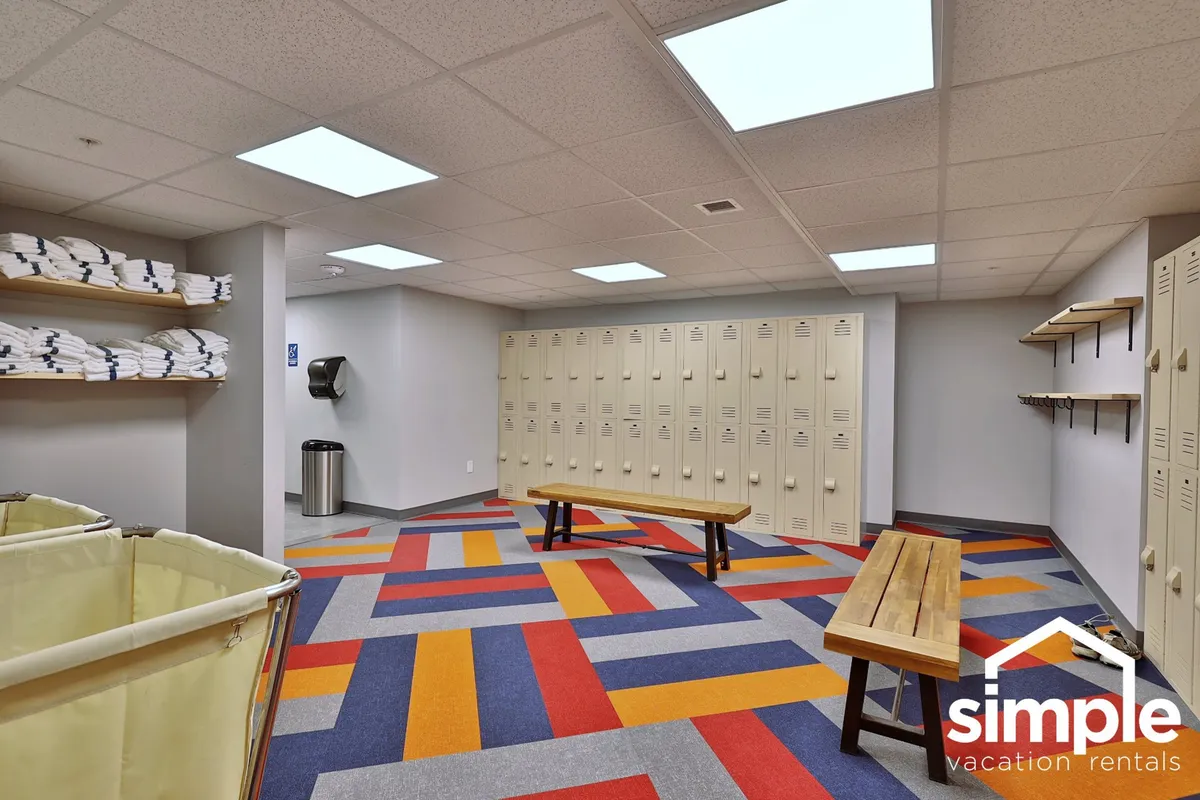 A vibrant locker and changing area with colorful geometric flooring, neatly arranged towels, lockers, and wooden benches. The space is practical for guests to transition between activities or refresh themselves after resort amenities like the pool or sauna.