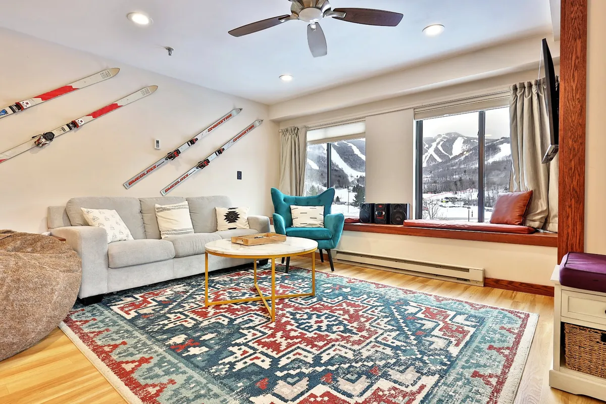 A stylish and comfortable living area with a sofa, decorative rug, window views, and ski equipment. The sofa serves as a central point for relaxation and can be used as a sofa bed for additional guests.