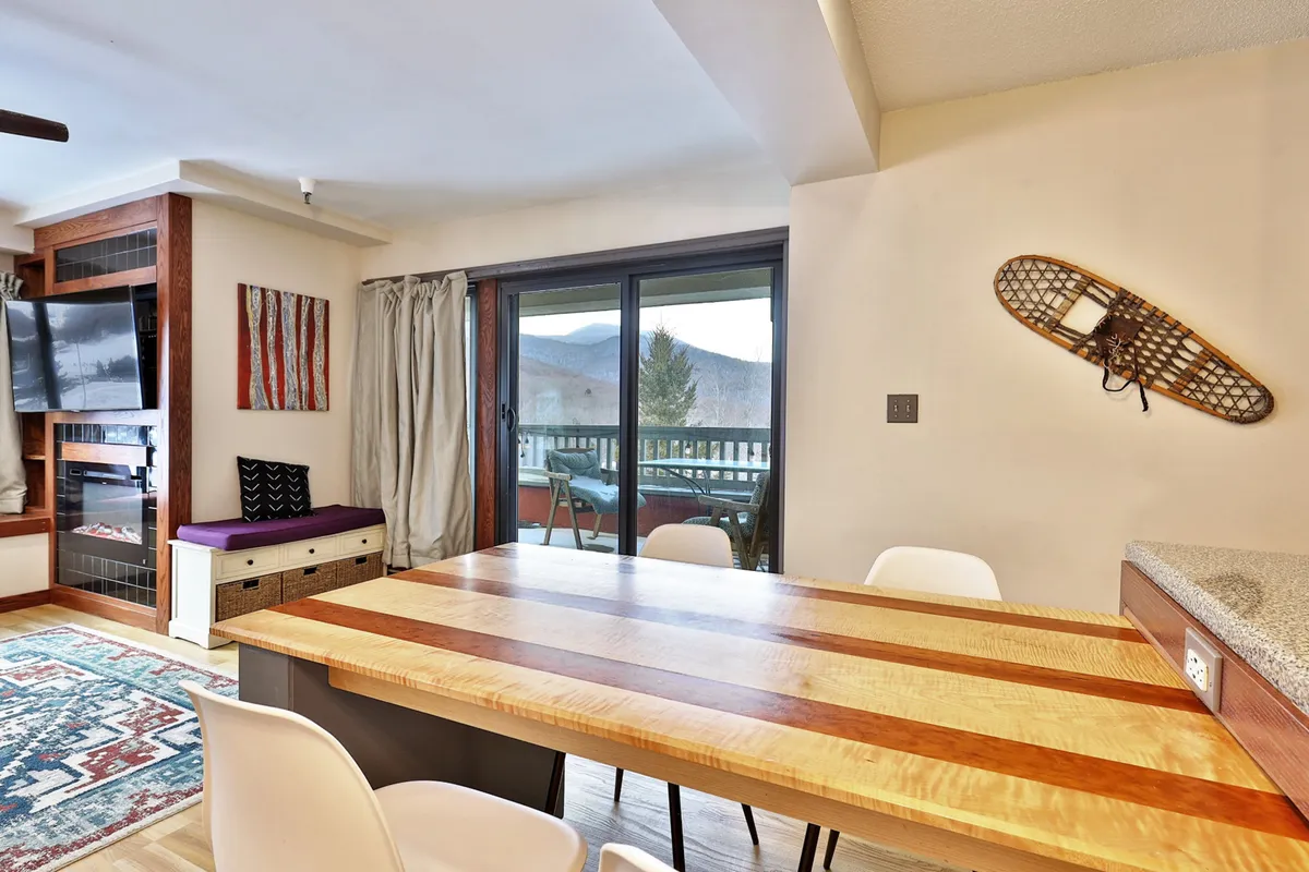 A cozy dining area featuring a wooden table set beside large windows that showcase glimpses of the mountain scenery outside. Decorative wall art and a snowshoe accent hint at local, outdoorsy themes, and the natural light streaming in suggests a close connection to the landscape beyond the home.