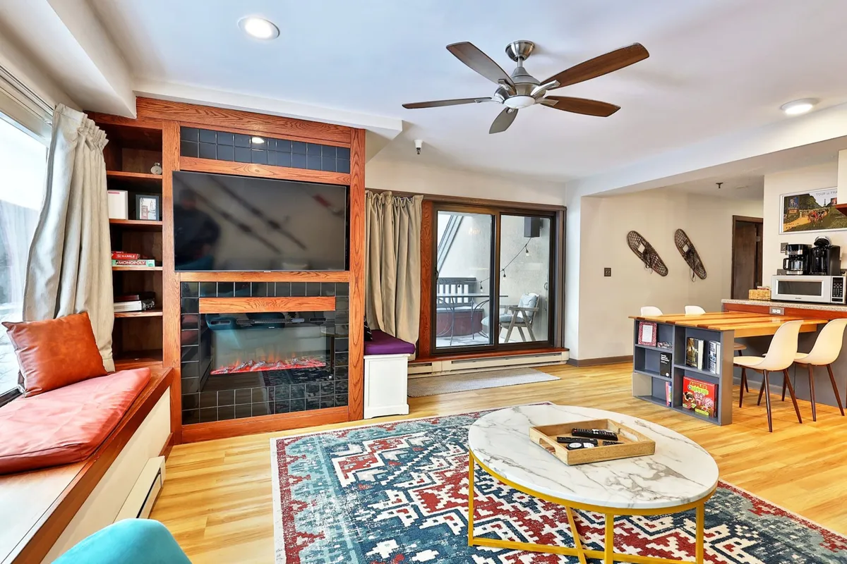 A sunlit, welcoming living area with a fireplace, a coffee table for casual work or play, window seating with a view, and a dining area—ideal for enjoying meals or collaborating over projects.