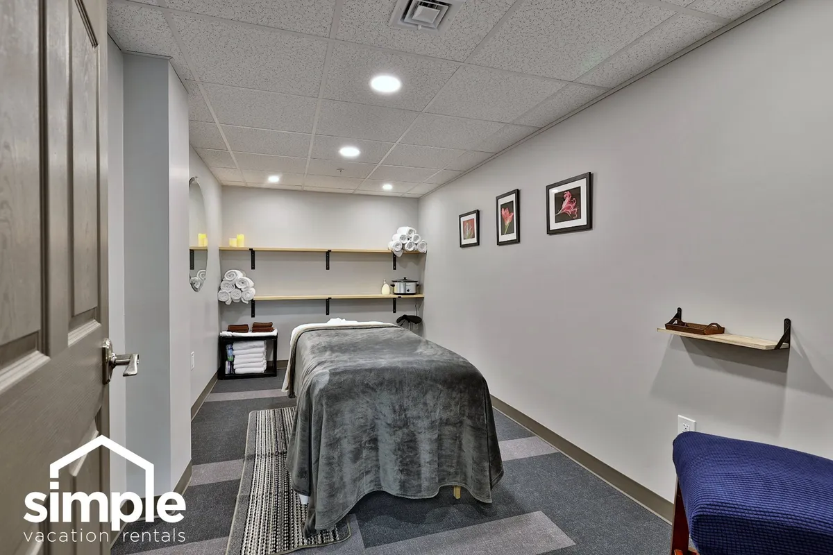 A serene massage room featuring a massage table, shelves with neatly arranged towels, and framed artwork. The mood is tranquil and spa-like, offering a visual of the relaxation awaiting guests after a day on the course.