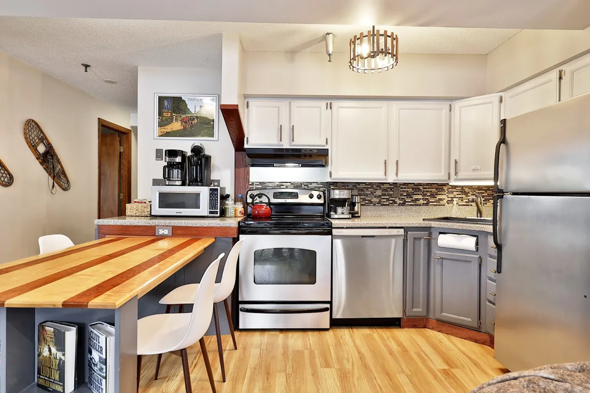 A warm, inviting kitchen space featuring a kitchen island, stainless steel appliances, colorful artwork, and wooden accents. The open design suggests ample space for cooking, entertaining, or gathering with family for meals.