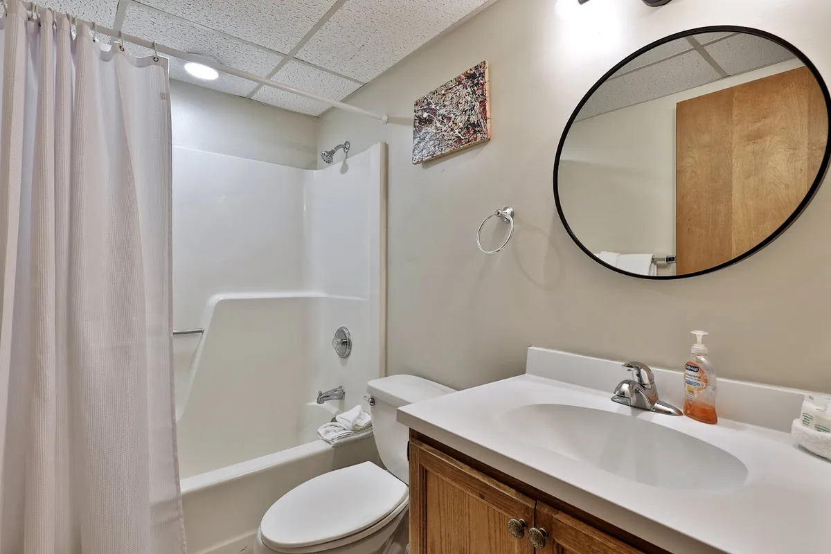 A modern, inviting bathroom with a round mirror, spacious sink, shower area, and tasteful wall art. It feels bright, clean, and practical for group use.