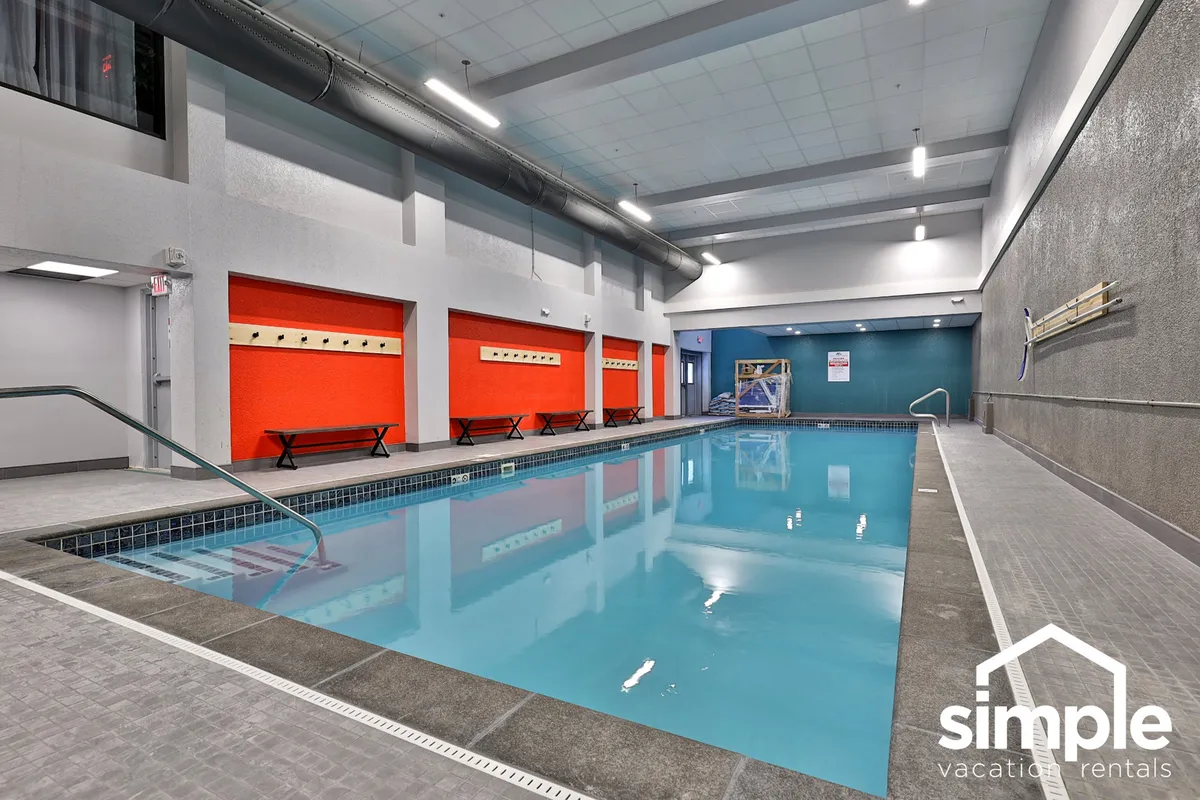 A vibrant indoor heated pool area with colorful wall accents and benches, inviting guests to relax and socialize after a day on the mountain. The bright setting suggests a family-friendly, refreshing retreat.